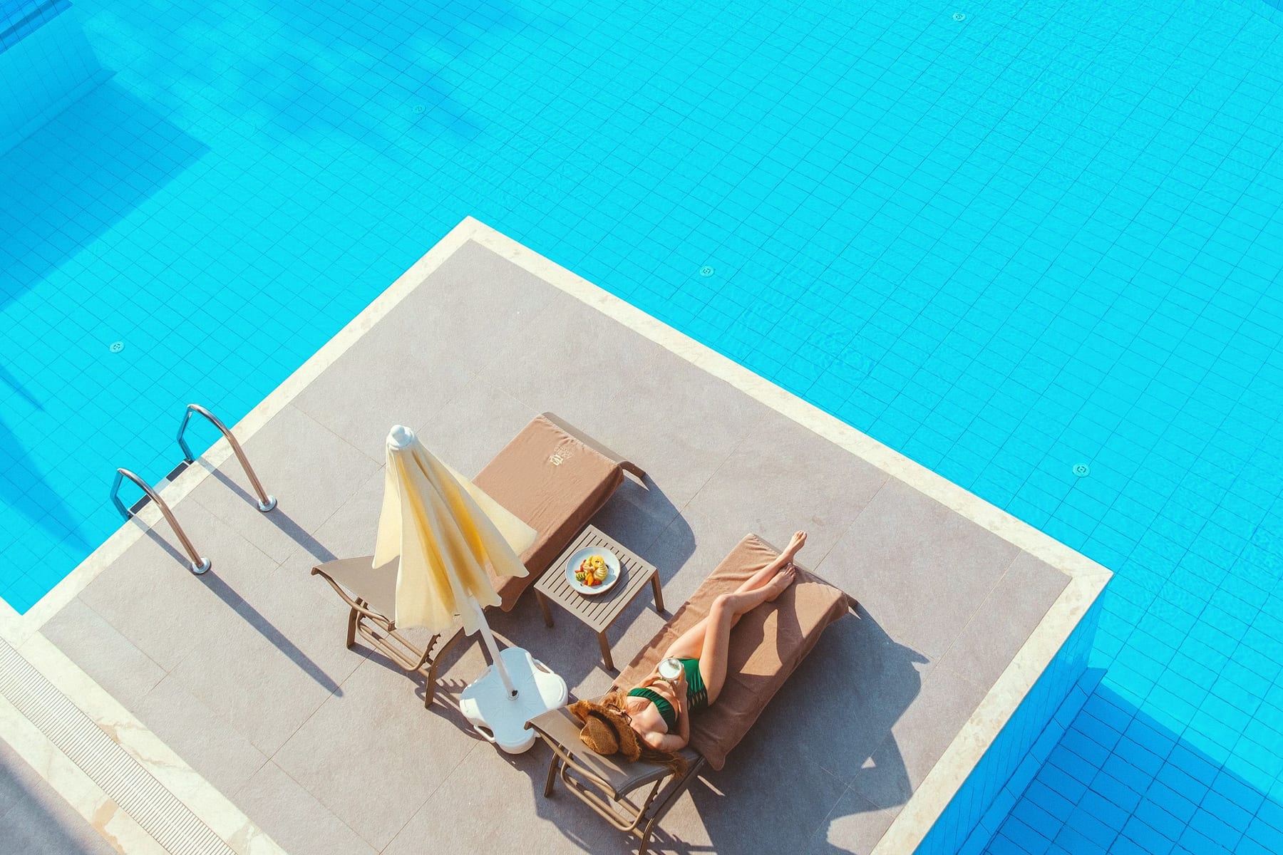 Piscine à l’eau turquoise vue du ciel, transats et parasol sur la terrasse en pierre